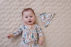 Baby lying on a quilted surface wearing Aster & Oak Organic Zip – Noah Woodland Onesie and hat.