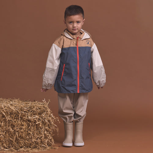 Child wearing the Crywolf Packable Jacket Ash Colourblock and pants standing next to a bale of hay on a brown background