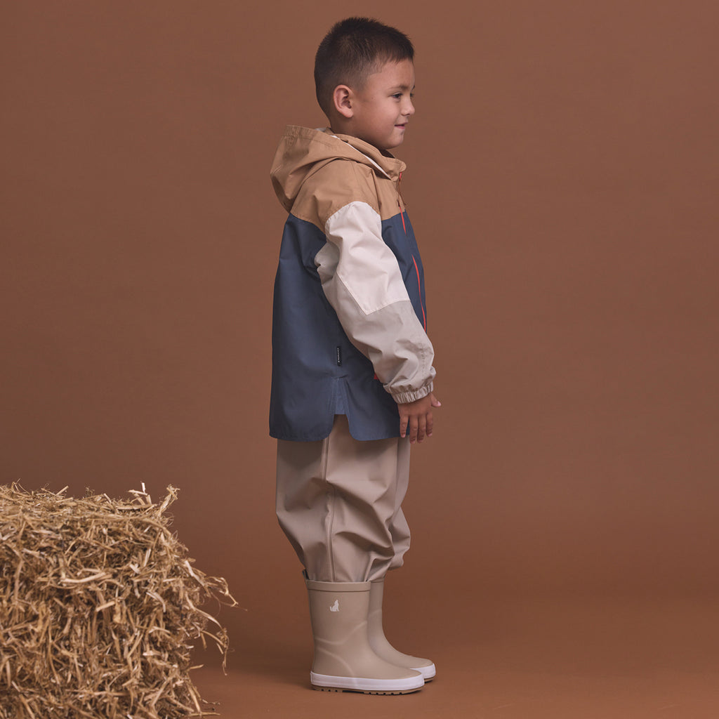 Child wearing the Crywolf Packable Jacket Ash Colourblock and pants standing next to a bale of hay on a brown background