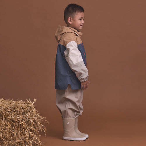 Child wearing the Crywolf Packable Jacket Ash Colourblock and pants standing next to a bale of hay on a brown background