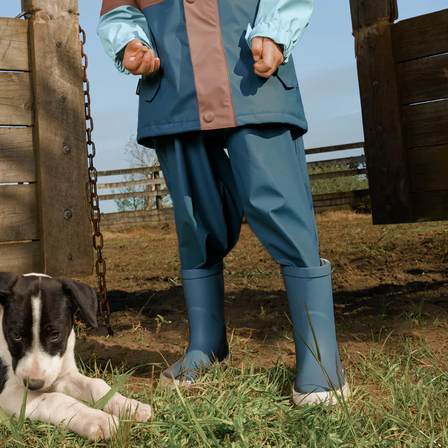 Person wearing blue raincoat and Crywolf Rain Boots Highland Blue standing next to a dog in an outdoor setting.