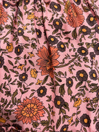 A close of up of Blush Wildflower Print, Pink floral fabric with a repeating pattern of brown, orange, and yellow flowers with leaves.