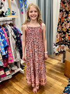 A young girl with blonde hair stands barefoot in a clothing store, wearing a sleeveless, MilaMeli Aria Spring Dress Blush Widflower Print.