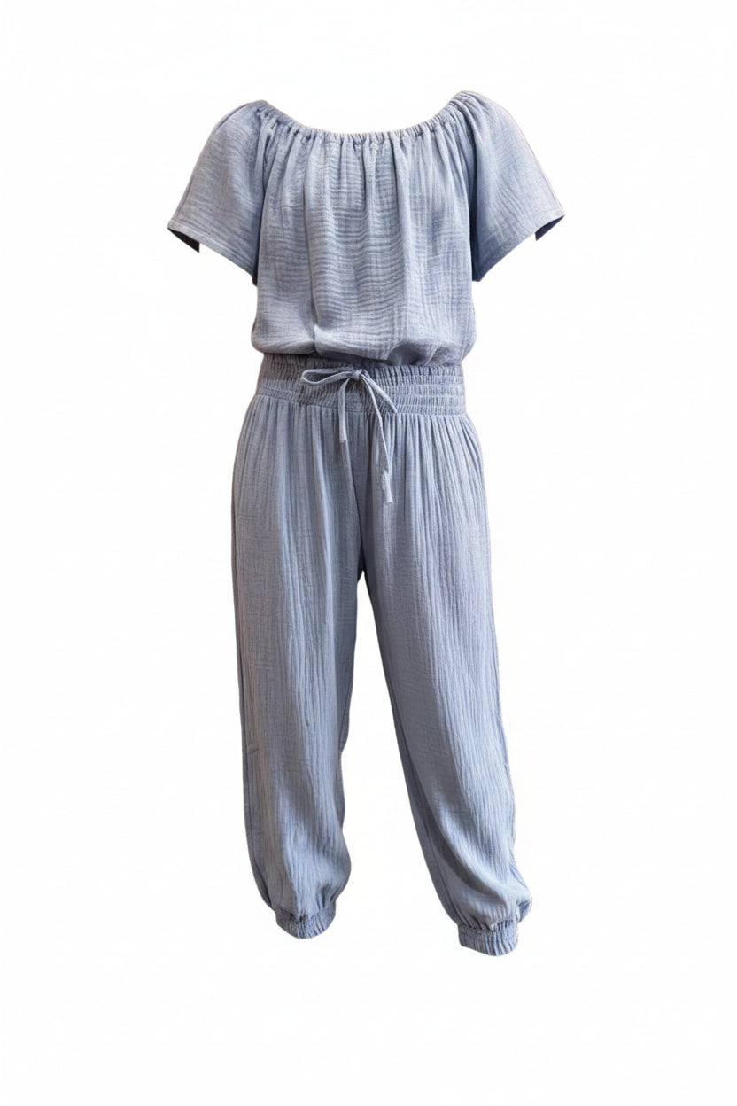 Light blue textured double-gauze short-sleeve jumpsuit featuring a smocked elastic waistband with a decorative drawstring and cinched ankles.