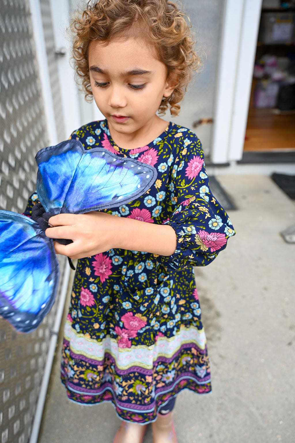 A young girl with curly light brown hair wearing Lotte Dress Indigo Wildflower top.