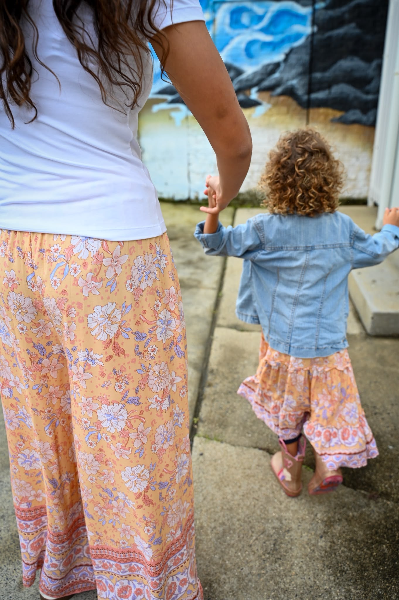 A woman and a young child walking hand in hand outdoors. The woman wears a white top and Mila Meli Lounge Pants Sunrise Botanica.